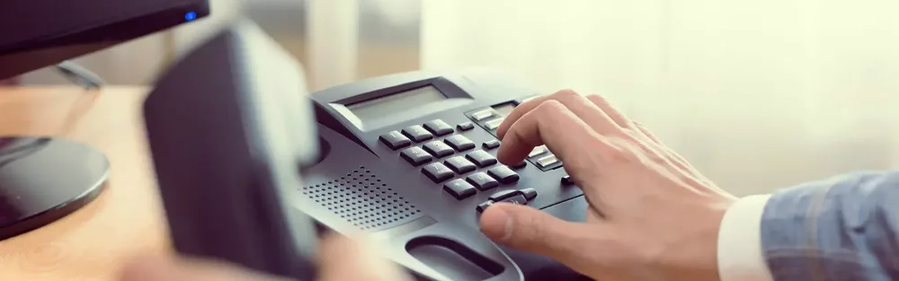 A hand dialing a desk phone